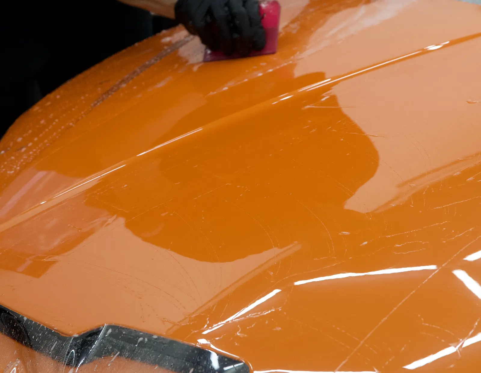 Profissional da The W aplicando PPF sobre o capô de um esportivo laranja